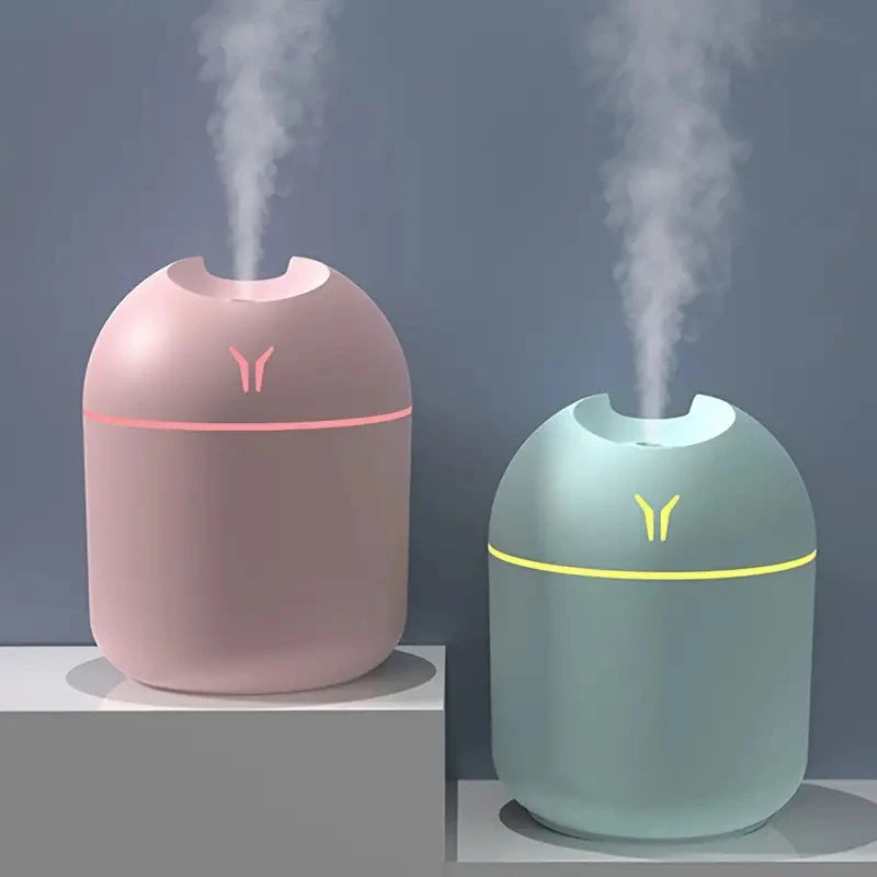 Pink and mint green ultrasonic humidifiers releasing steam, with illuminated accent rings and minimalist design, displayed on white platforms.